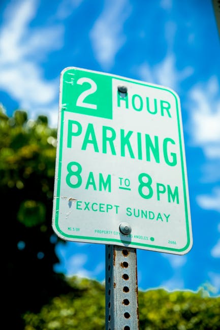 A green and white parking restriction sign mounted on a metal pole outdoors, indicating a two-hour parking limit from 8 am to 8 pm, except on Sundays. The sign has a black bolt at the top and bottom s
